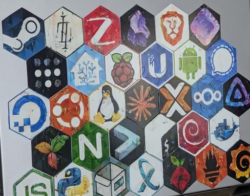 Hexagonal mosaic stickers arranged in a honeycomb pattern on metal, featuring open source and tech logos including Tux, Ubuntu, Raspberry Pi, Home Assistant, Debian, Android, and others. Each design has a triangular mosaic texture.