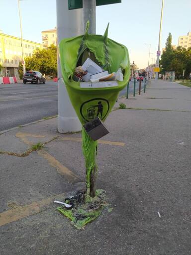 a melted trash can with a cigarette bin barely holding onto it